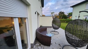 A patio with wicker furniture, a glass table, and a hanging chair. - Ferienwohnungen im Grund 22 (Hoppegarten)