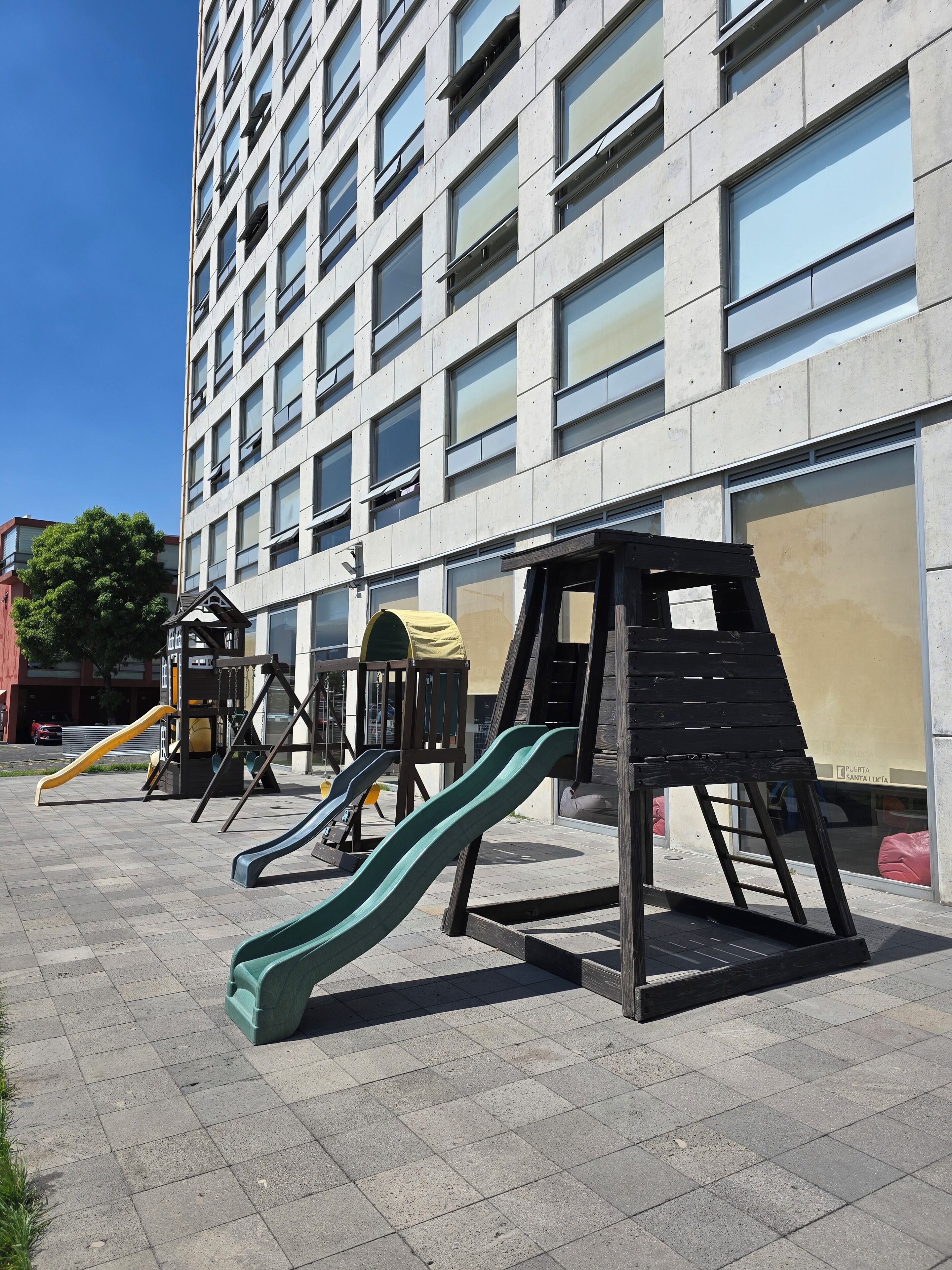 Un parque infantil con toboganes y estructuras para escalar frente a un edificio con grandes ventanales.
