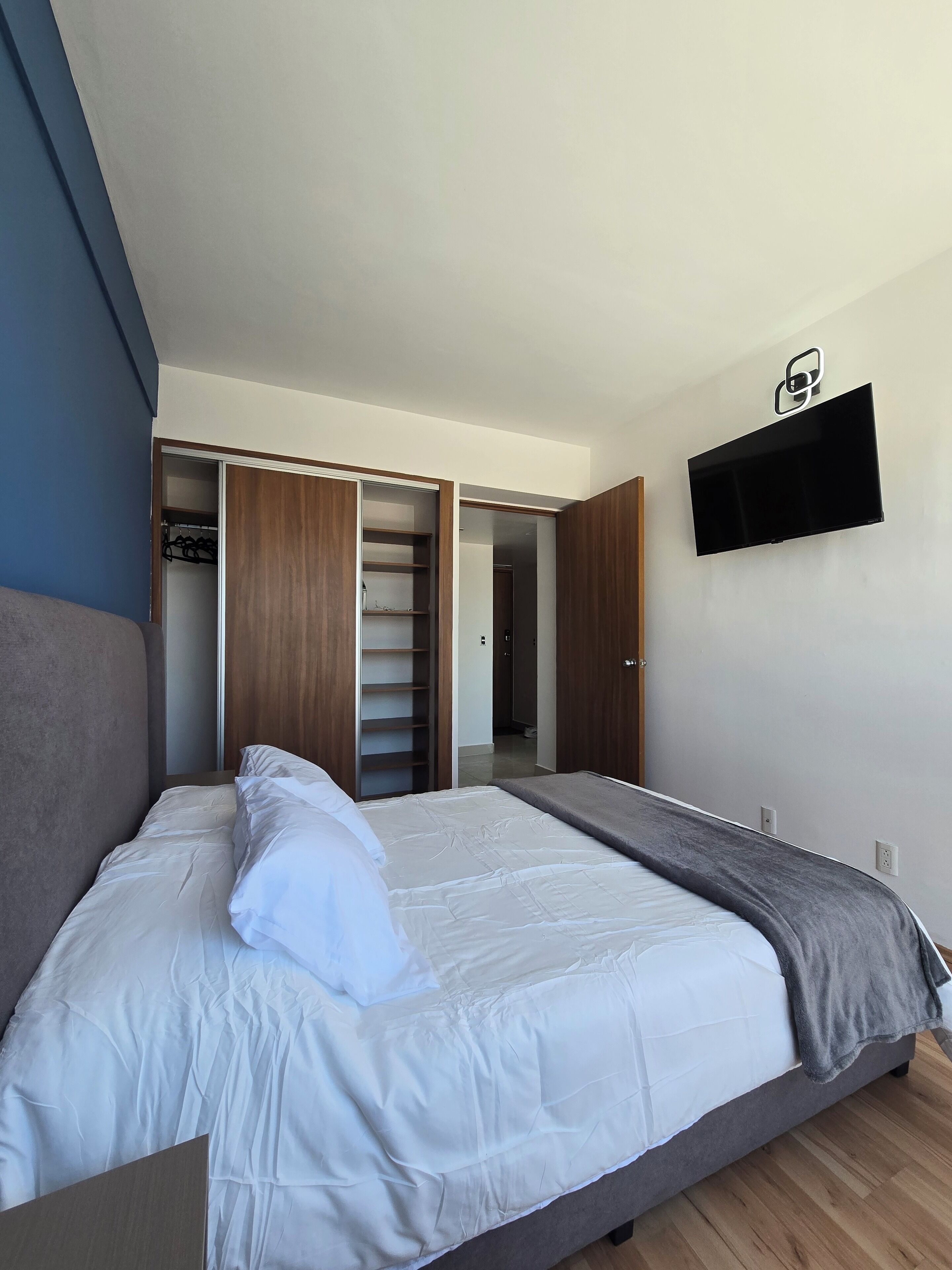 A bedroom with a bed, a wardrobe, and a TV mounted on the wall.