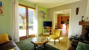 A living room with a sofa, a coffee table, a TV, and a fireplace. There is a kitchen visible through an open door. - 4-bedroom villa, nature, quiet, panoramic mountain views (Salles-et-Pratviel (31110))