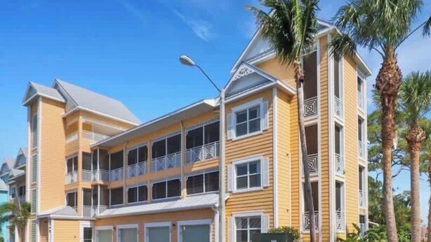 A multi-story hotel with balconies, a parking lot, and palm trees.
