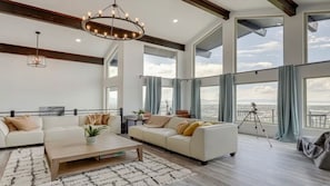 A spacious living room with a large window offering a view of the sea, a modern chandelier, and a tripod in the corner. - Panoramic Luxury Estate - Refined 30+ Night Stays (Provo)