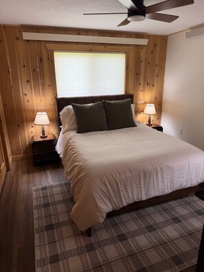 Ein Schlafzimmer mit einem Bett, zwei Nachttischen mit Lampen, einem Deckenventilator und einem karierten Teppich.