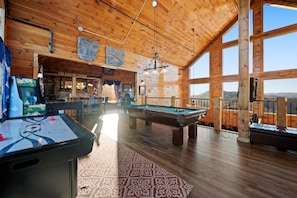 Un intérieur en bois avec des tables de billard, un coin bar et de grandes fenêtres offrant une vue dégagée.