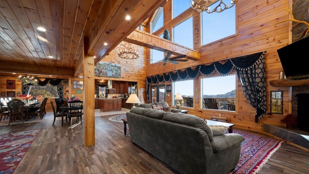 A spacious wooden cabin interior with a dining area, sofa, and fireplace. - 360° Mountaintop Views | Hogwarts Room, 19-Seat Theater & 2 Pubs (Sevierville)