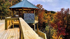 A wooden deck with a stone wall and a metal-roofed pavilion overlooking a forested hillside. - 360° Mountaintop Views | Hogwarts Room, 19-Seat Theater & 2 Pubs (Sevierville)