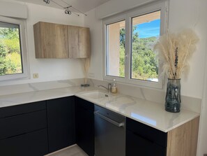 A modern kitchen with a dishwasher, a sink, and a window with a view of greenery. - House with swimming pool and 5 bedrooms (Porto-Vecchio)