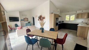 Een moderne keuken met een eethoek, met een houten tafel en stoelen, een flatscreen televisie en een groot raam.