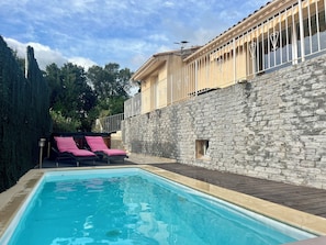 Una piscina con un muro de piedra y un balcón con barandilla de metal.