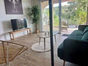A modern living room with a flat-screen TV, a wooden bench, a round table with glasses, a green sofa, and a large potted plant. - House with swimming pool and 5 bedrooms (Porto-Vecchio)