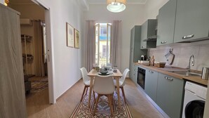 A modern kitchen with a built-in washing machine, a dining area with a table and chairs, and a view through a window. - Marèa - Holiday House (Santa Flavia)