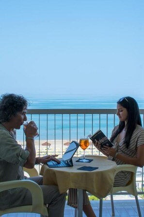 Two people seated at a table with a laptop and a book, overlooking a beach. - Hotel Atlantic (Giulianova)