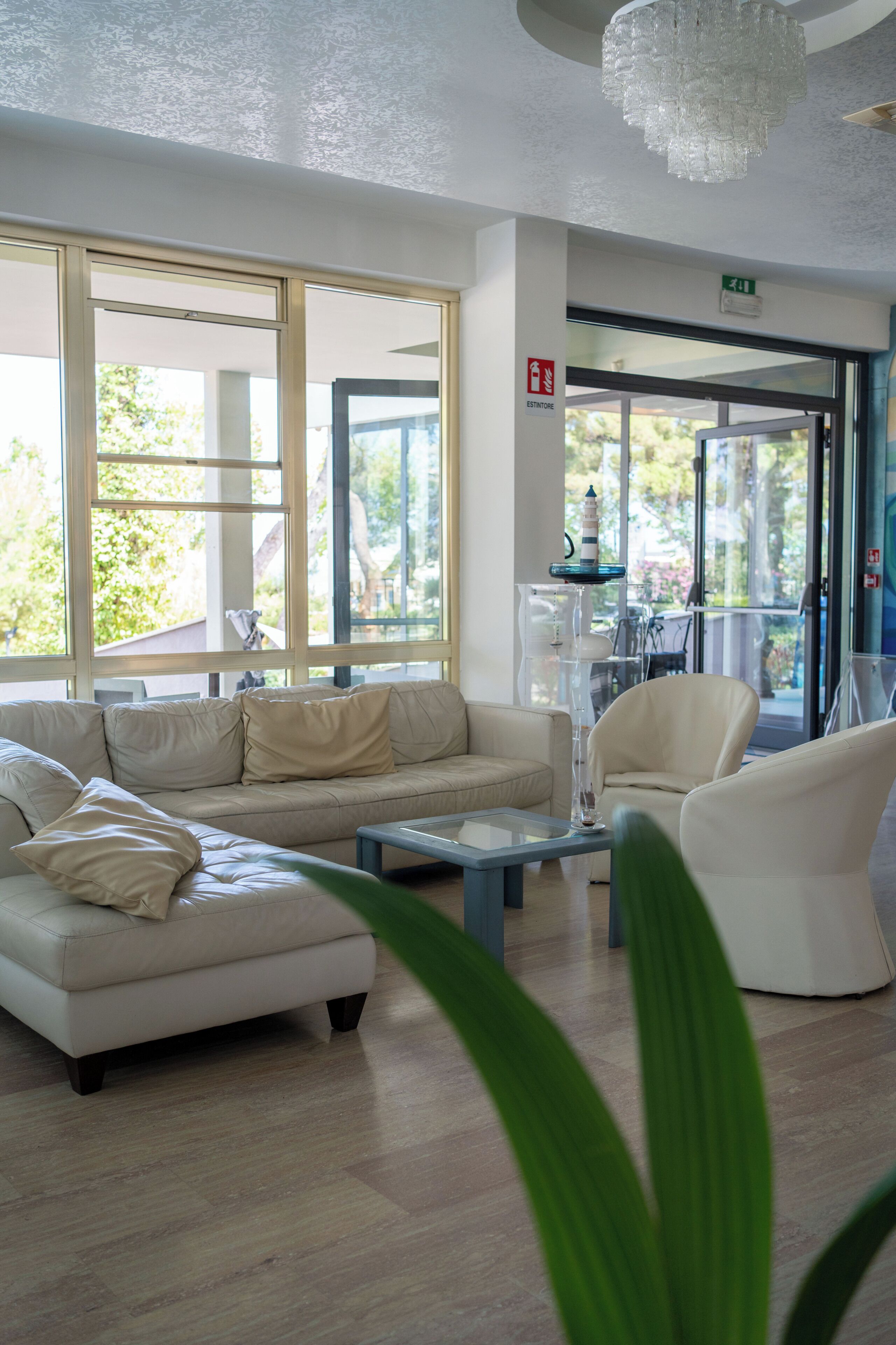A modern hotel lobby with a sofa, armchairs, a coffee table, and large windows offering a view of the outdoors.