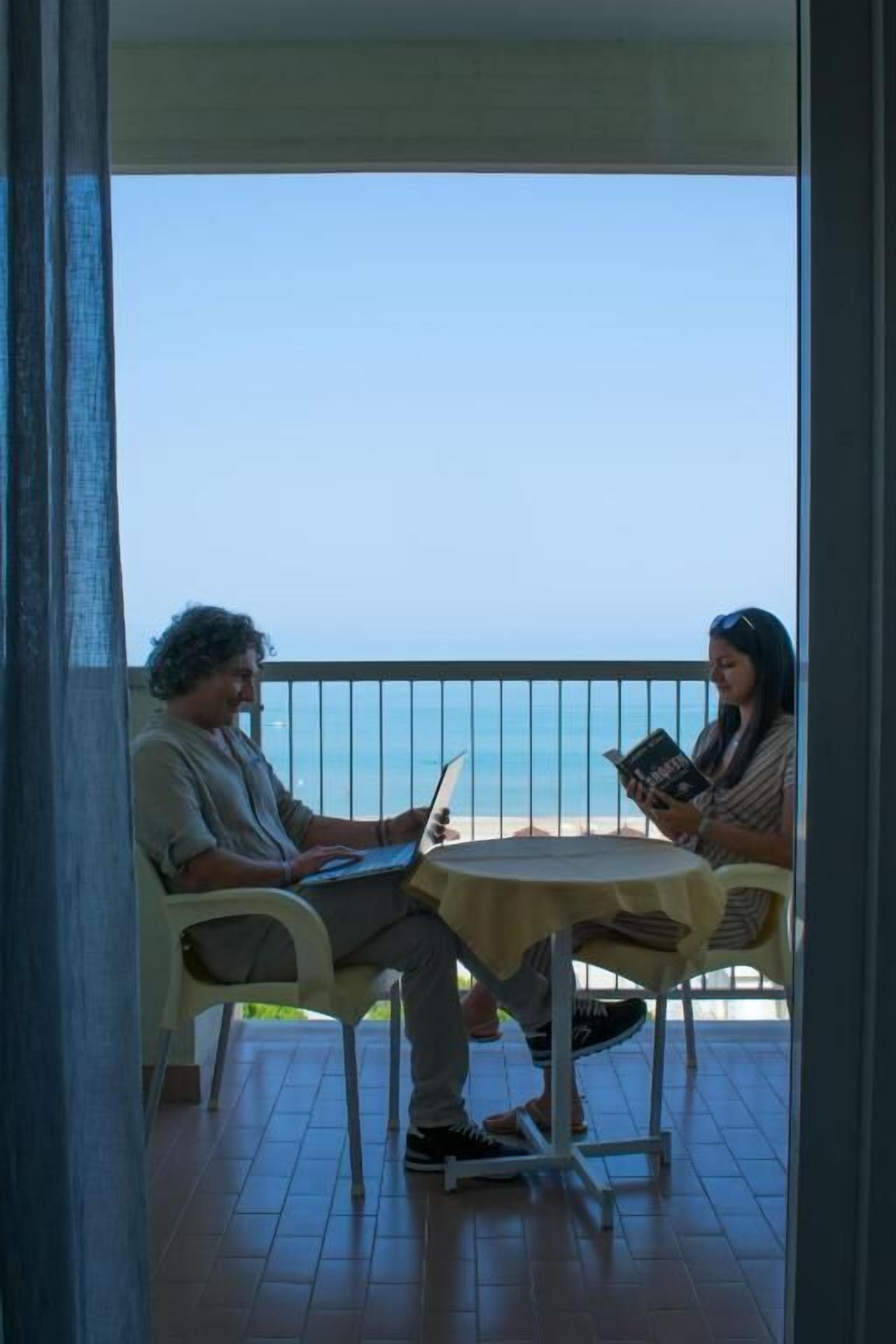 A balcony with two chairs, a table, and a view of the sea.