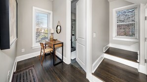 Un couloir avec un bureau en bois, une chaise et une fenêtre avec des stores.