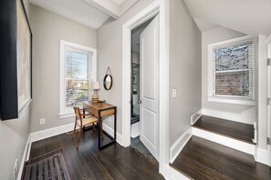 A hallway with a wooden desk, a chair, and a window with blinds. - Step into the coziest two bedroom! (Columbus)