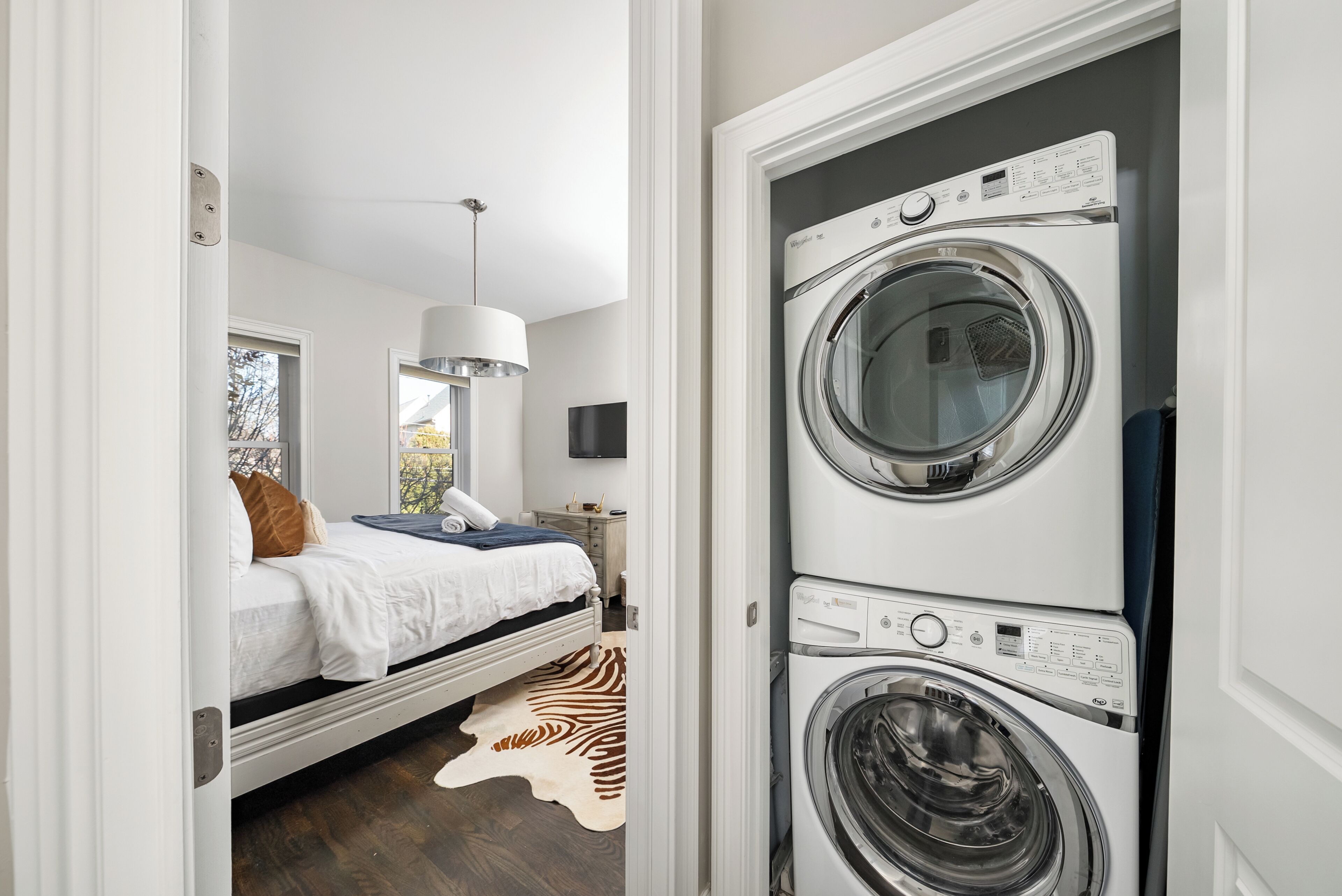 A bedroom with a bed, a zebra rug, a hanging light, and a wall-mounted TV.