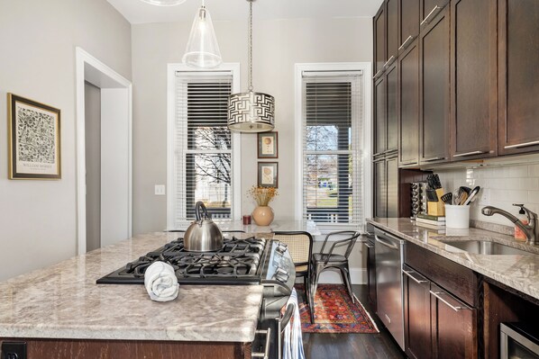 A kitchen with a central island, stainless steel appliances, dark wooden cabinets, and a hanging pendant light. - Step into the coziest two bedroom! (Columbus)