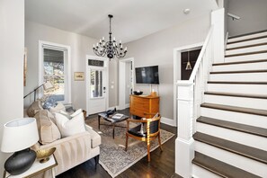 A living room with a sofa, coffee table, chandelier, and a staircase. - Step into the coziest two bedroom! (Columbus)