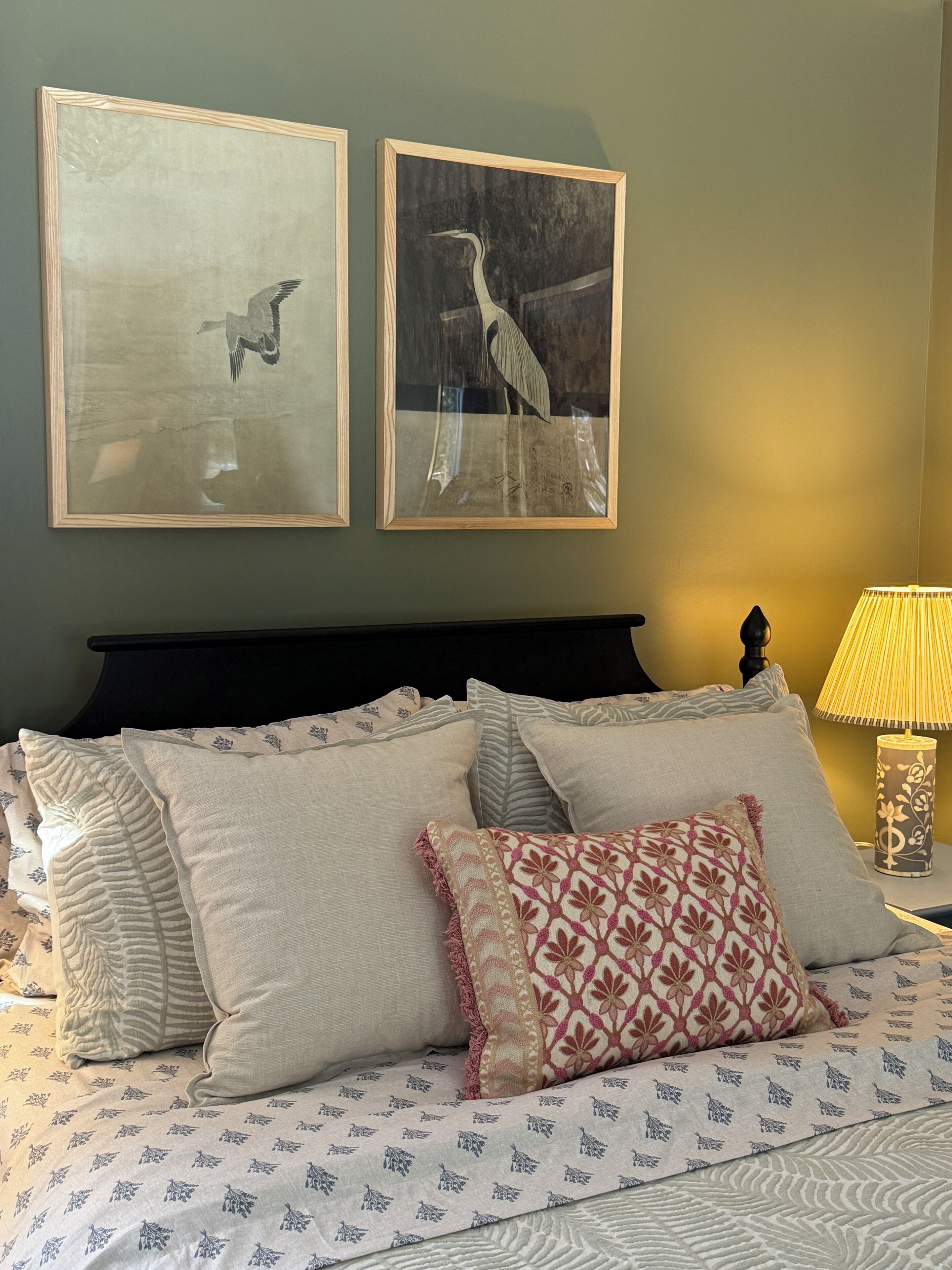 A neatly made bed with patterned bedding, a dark headboard, and two framed wall art pieces depicting birds.