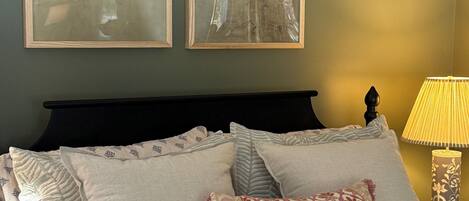 A neatly made bed with patterned bedding, a dark headboard, and two framed wall art pieces depicting birds.