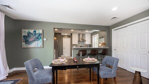A dining area with a dark wooden table, two grey upholstered chairs, and a white round table. - Blue Lotus, LUXE Cottage, in walkable Kennett Square near Longwood Gardens (Kennett Square)