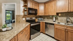 A kitchen with wooden cabinets, granite countertops, a microwave, stove, oven, dishwasher, and a sink.