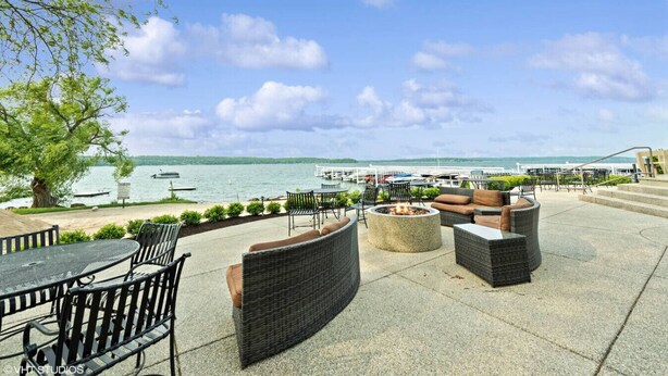 An outdoor patio with wicker furniture, a fire pit, and a view of the lake and marina.