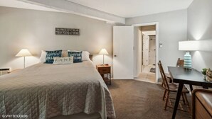 A bedroom with a bed, two bedside lamps, a nightstand, a wall-mounted sign, and a door leading to a bathroom.