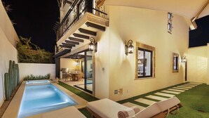 Un espace piscine extérieur moderne, doté de chaises longues, d’un escalier et d’un intérieur bien éclairé.
