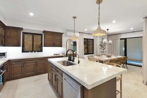 Une cuisine spacieuse dotée d’un grand îlot central, de meubles en bois et d’un éclairage moderne suspendu au plafond.