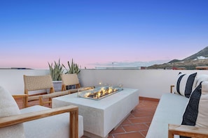 Une terrasse sur le toit avec une table à plateau en verre, des chaises en osier et un canapé agrémenté de coussins à rayures.