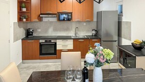 A modern kitchen with wooden cabinets, a built-in oven, a stainless steel refrigerator, and a dining area with a marble table and chairs. - Villa  Ika (Raščane)