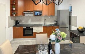 Une cuisine moderne avec des meubles en bois, un four encastré, un réfrigérateur en acier inoxydable et un coin repas avec une table et des chaises en marbre.