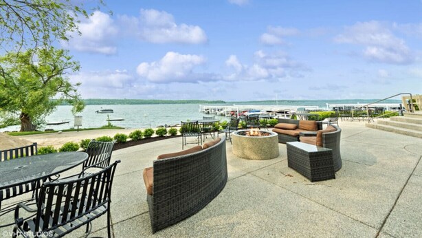 An outdoor patio with wicker furniture, a fire pit, and a view of the marina and lake. - Deerpath Retreat at Abbey Springs (Fontana-on-Geneva Lake)