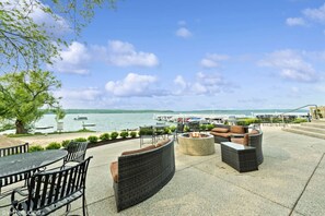 An outdoor patio with wicker furniture, a fire pit, and a view of the marina and lake. - Deerpath Retreat at Abbey Springs (Fontana-on-Geneva Lake)