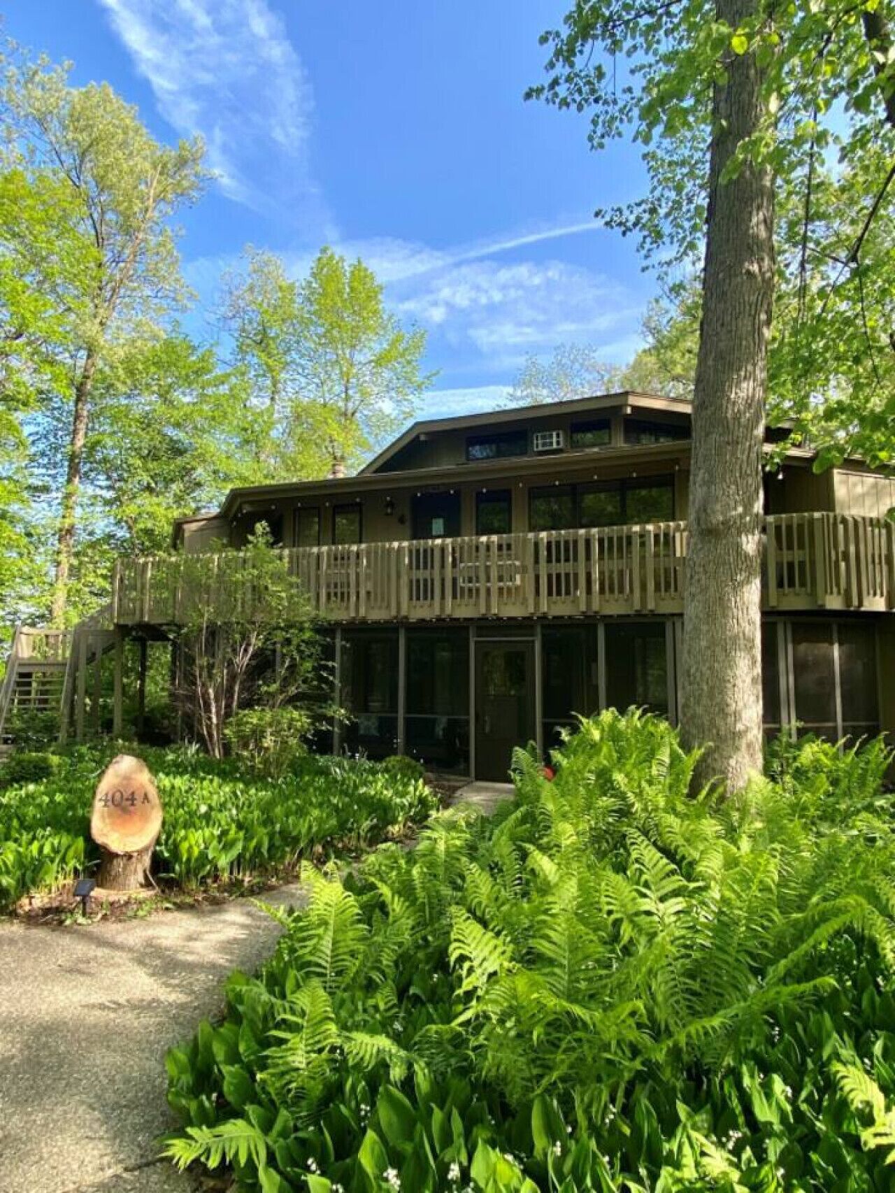 Un bâtiment à deux étages doté d’une terrasse en bois, entouré d’une végétation luxuriante et d’arbres.