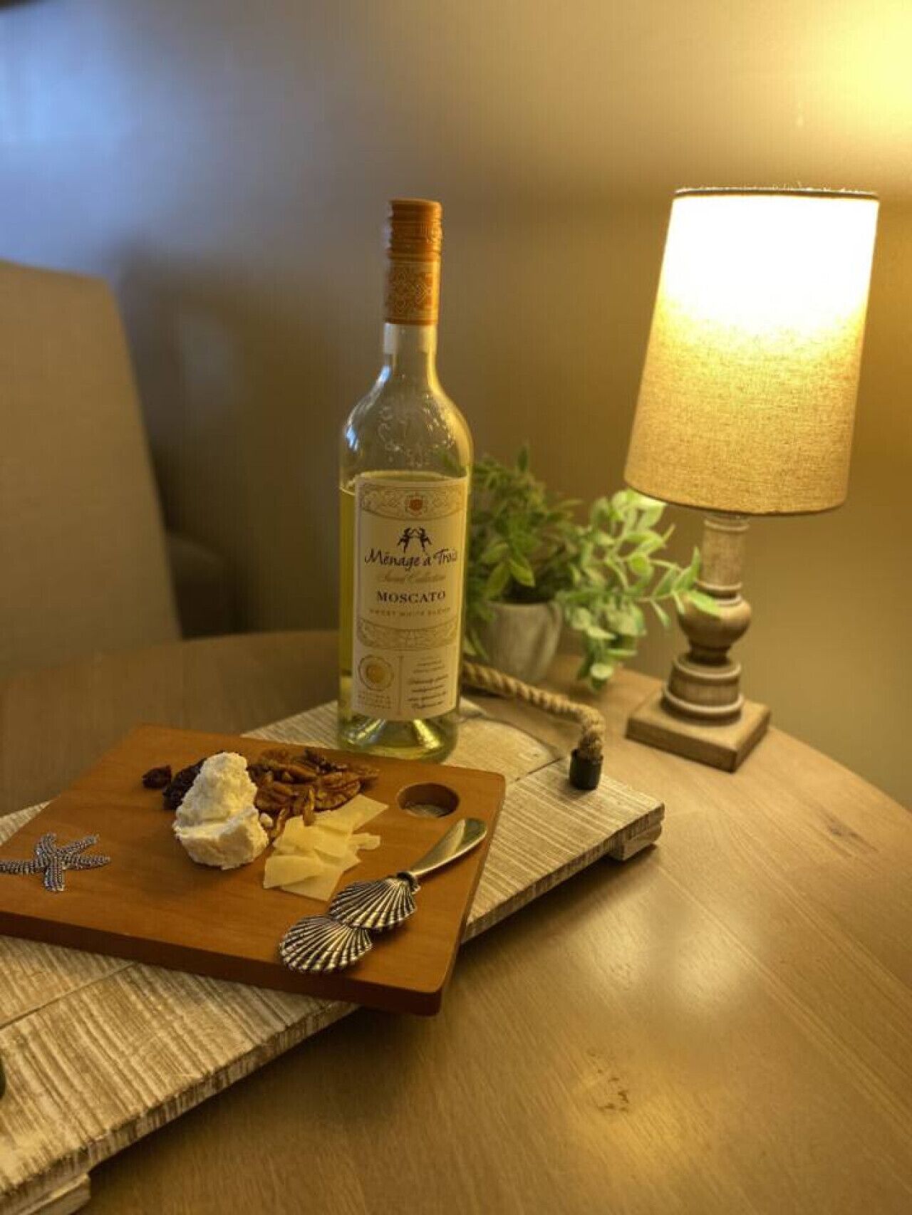 Una botella de vino sobre una tabla de madera con queso, galletas, una cuchara y una decoración de estrella de mar.