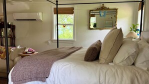 Een bed met hemel, een nachtkastje met lamp, een raam met uitzicht en een airconditioning.