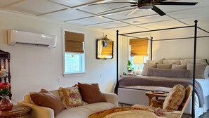 Een kamer met een plafondventilator, een bed met hemelbed, een bank, een stoel met bloemenstof bekleding, en een rieten mand op de vloer.