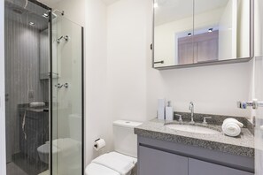 A modern bathroom with a glass shower enclosure, a white toilet, and a granite countertop sink. - StayHome Vila Clementino com Academia (São Paulo)