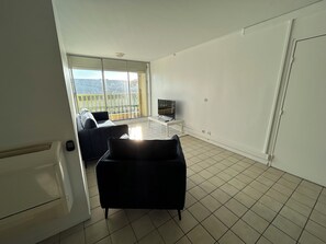 A spacious living room with a large window, a flat-screen TV, and a black sofa.
