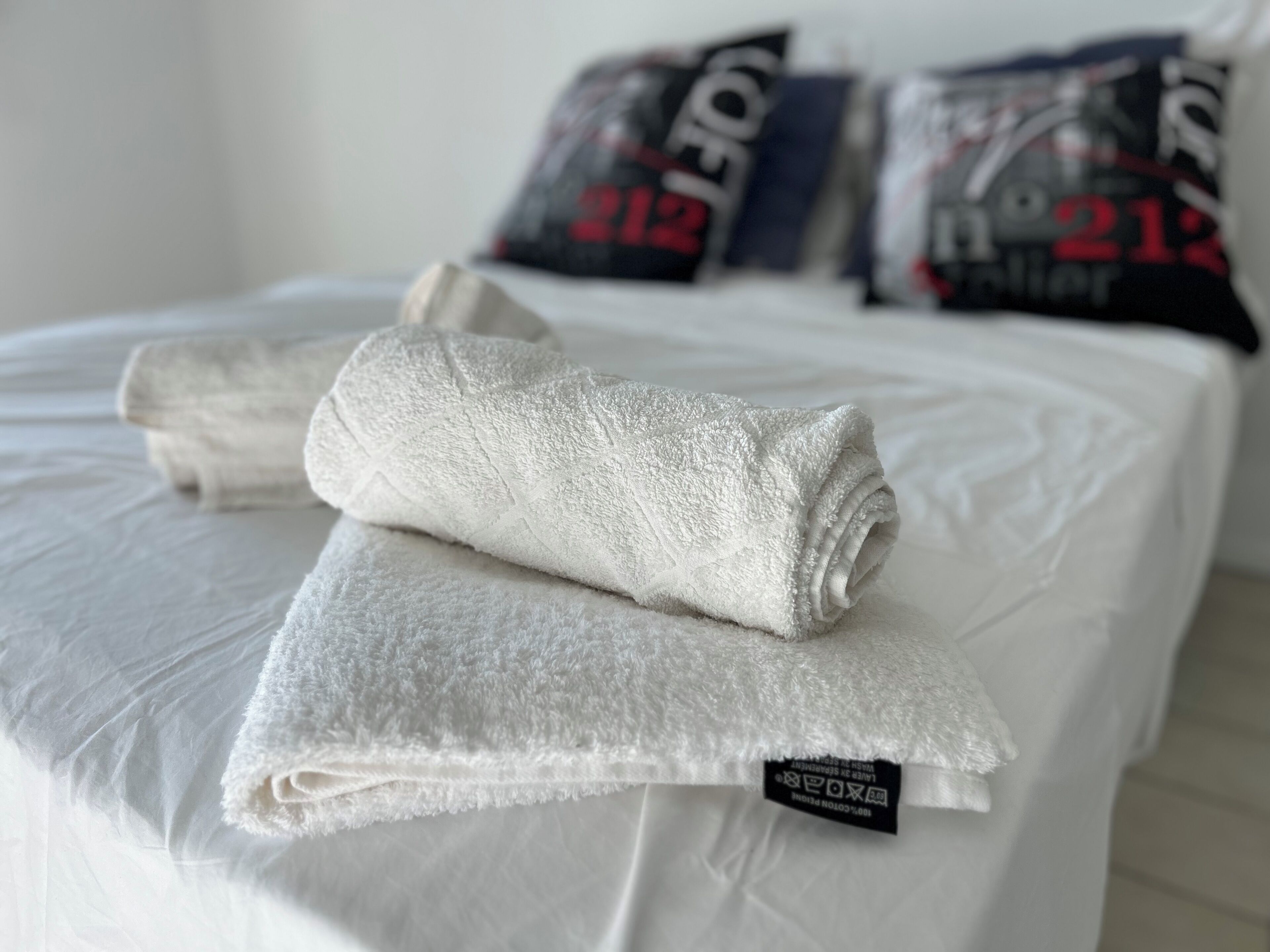A neatly made bed with white bedding and a rolled towel on top.
