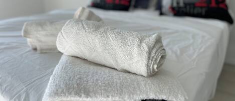 A neatly made bed with white bedding and a rolled towel on top.