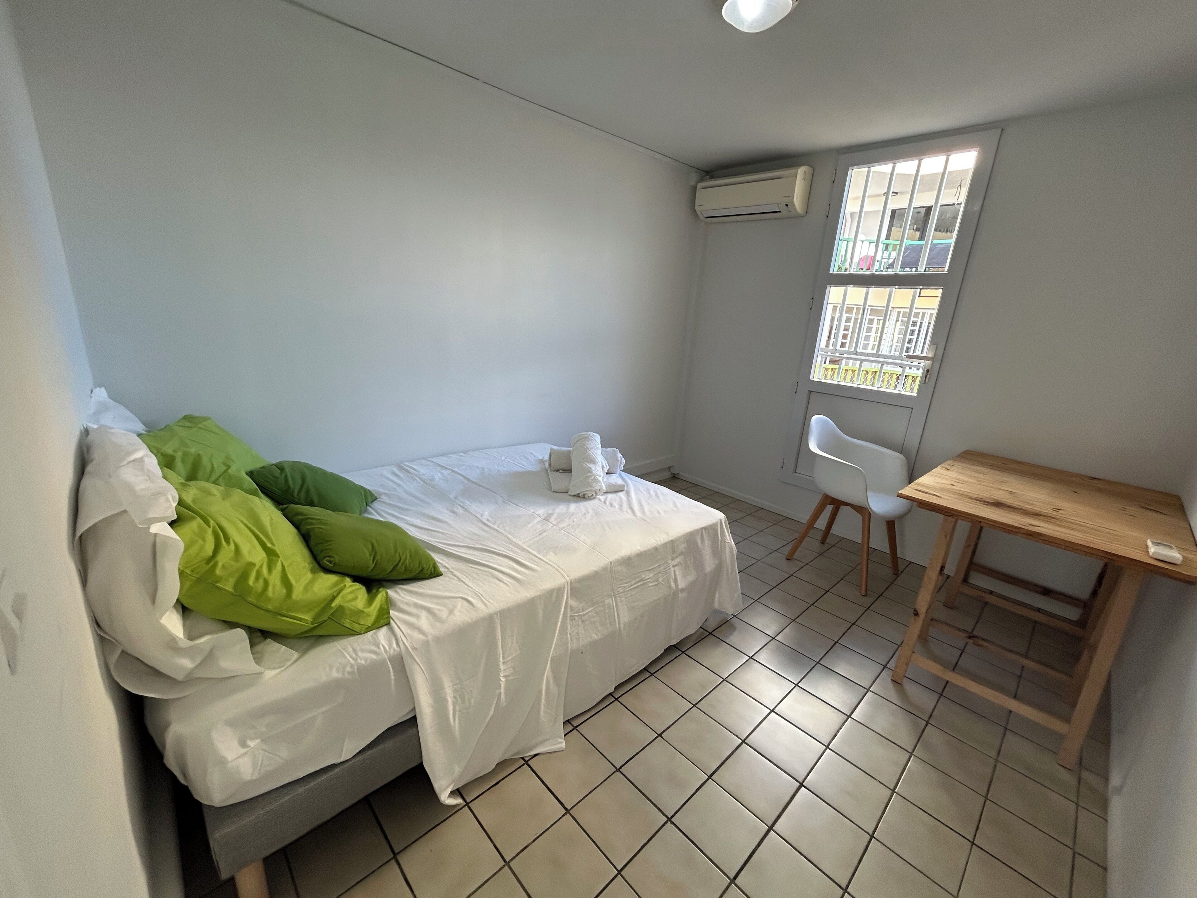 Une petite pièce propre, avec un lit, un bureau et une fenêtre.