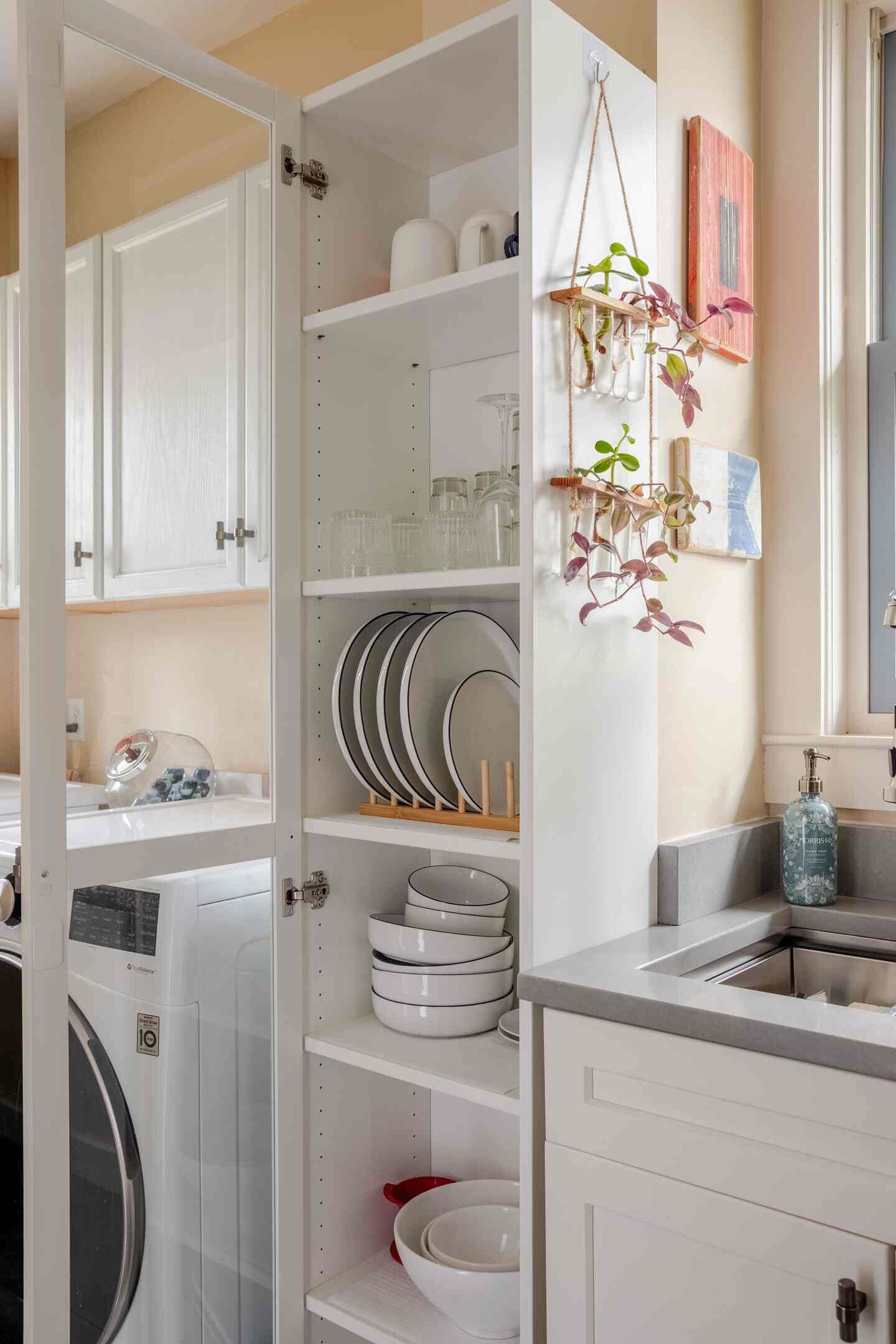 Cocina con alacenas blancas, lavadora y una planta colgante.