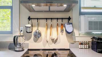 Una cocina con extractor de acero inoxidable, utensilios colgantes, un hervidor y un especiero.