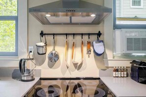 Uma cozinha com coifa de aço inoxidável, utensílios pendurados, chaleira e um porta-temperos.