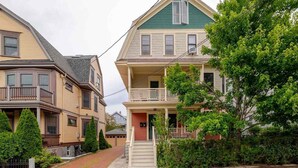 A row of two-story houses with front porches and a tree in the foreground. - Classic charm with modern comforts near Harvard. (Cambridge)