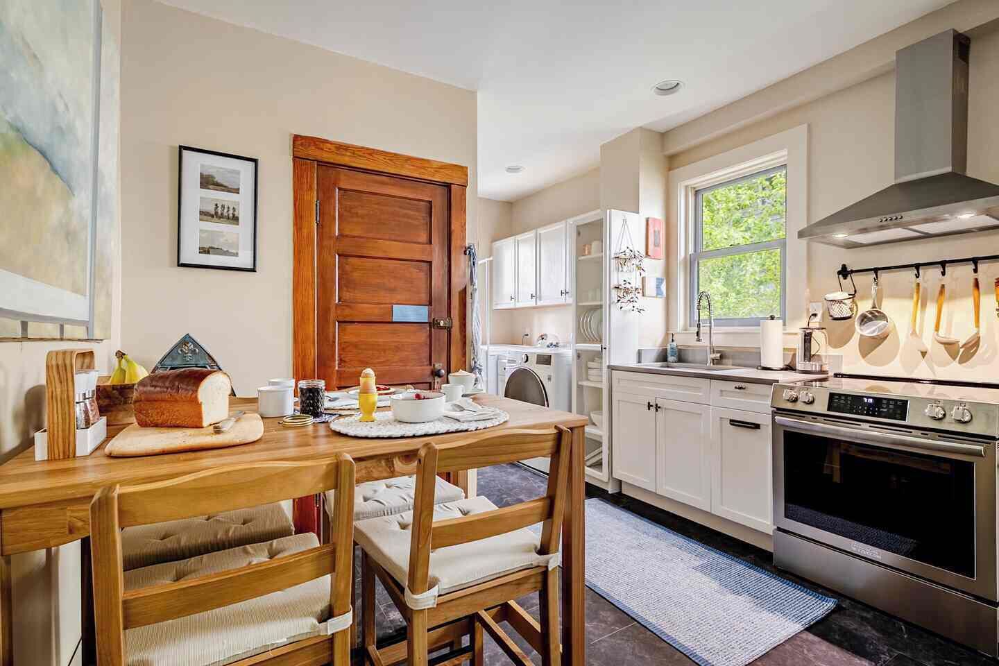 Una cucina moderna con tavolo da pranzo in legno, mobili bianchi ed elettrodomestici in acciaio inossidabile.